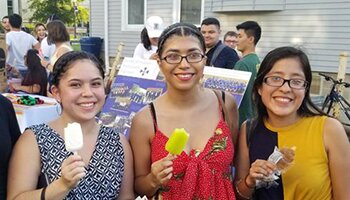 Three women smile while holding ice cream bars at an event outside of La Casa.