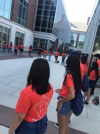 Large group of Conéctate participants in orange shirts doing an outdoor group activity