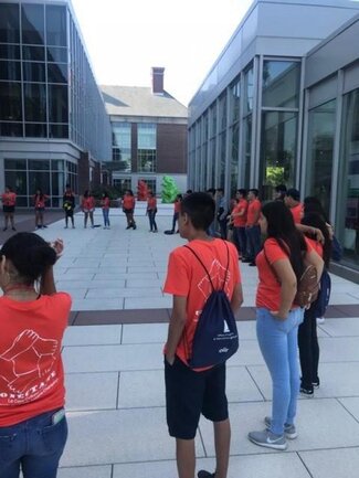 Large group of Conéctate participants in orange shirts doing an outdoor group activity
