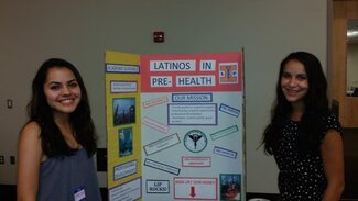 Two women standing on either side of information board about Latinos in Pre-Health