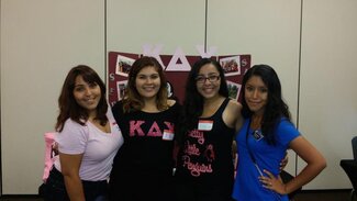 Four sorority members wearing their chapter apparel in front of display board