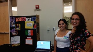 Two students standing next to display board and laptop screen