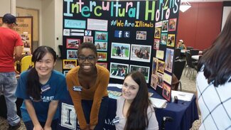 Three women posing in front of Intercultural Horizons display board