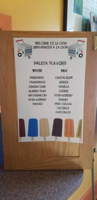 Menu poster of paleta flavors hanging on door at La Casa