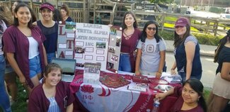 Group of seven students from Lambda Theta Alpha standing around information table outside of La Casa