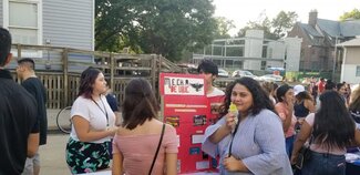 Woman eating paleta at information table with students in the background