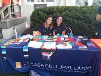 Two students seated behind a La Casa information table full of information materials and give-away items