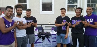 Six students showing their fraternity sign and wearing apparel while working at information table