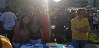 Small group of students working behind an information table with crowd in background