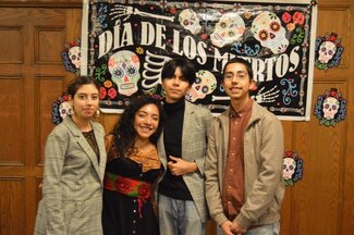 Four students smiling and posing in front of Día De Los Muertos banner