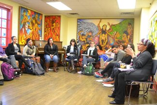 Group of attendees seated in circle listening at La Casa with colorful wall paintings in background